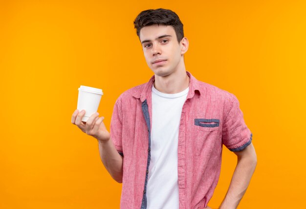 caucasian young man wearing pink shirt holding cup of coffee on isolated orange wall