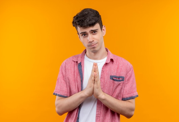 Free photo caucasian young man wearing pink shirt showing pray gesture on isolated orange wall