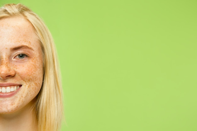 Free Photo caucasian young woman's close up portrait on green wall. female model in yellow shirt with blonde hair and freckles. concept of human emotions, facial expression.