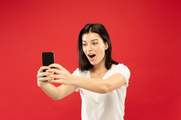 Caucasian young woman's half-length portrait on red studio