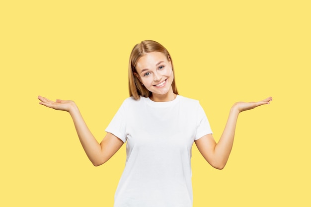 Caucasian young woman's half-length portrait on yellow studio background. Beautiful female model in white shirt