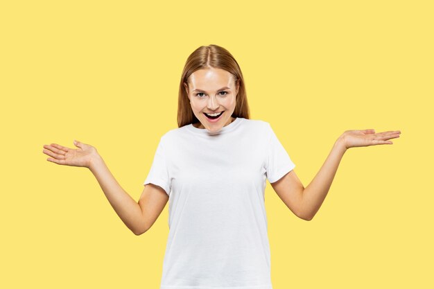 Caucasian young woman's half-length portrait on yellow studio background. Beautiful female model in white shirt