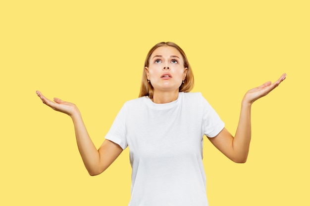 Caucasian young woman's half-length portrait on yellow studio background. Beautiful female model in white shirt