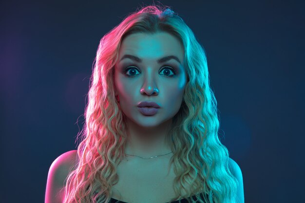 Caucasian young woman's portrait on gradient background in neon light. Beautiful female model with unusual look. Concept of human emotions, facial expression, sales, ad. Looks serious and calm.