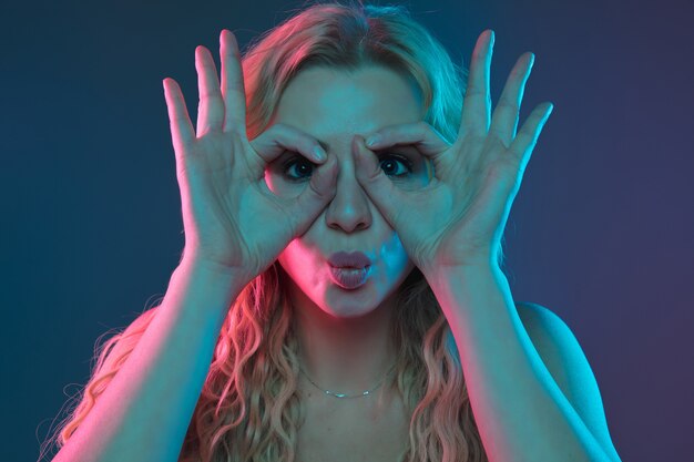 Caucasian young woman's portrait on gradient background in neon light. Beautiful female model with unusual look. Concept of human emotions, facial expression, sales, ad. Pointing, smiling. Copyspace.