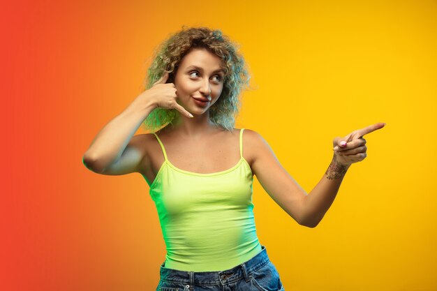 Caucasian young woman's portrait isolated on gradient studio background in neon. Beautiful female curly model in casual style. 