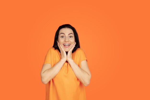 Caucasian young woman's portrait on orange  space. Beautiful female brunette model in shirt