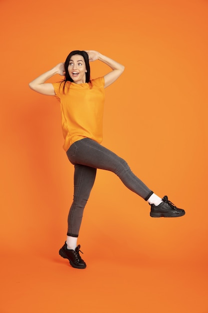 Caucasian young woman's portrait on orange  space. Beautiful female brunette model in shirt