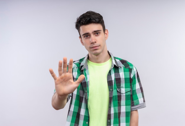 caucasion young man wearing green shirt showing stop gesture on isolated white wall