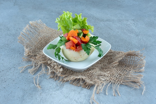 Cauliflower underneath parsley leaves, lettuce and chopped vegetables on a platter on marble table.