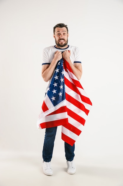 Free photo celebrating an independence day. stars and stripes. young man with flag of the united states of america isolated on white studio wall. looks crazy happy and proud as a patriot of his country.