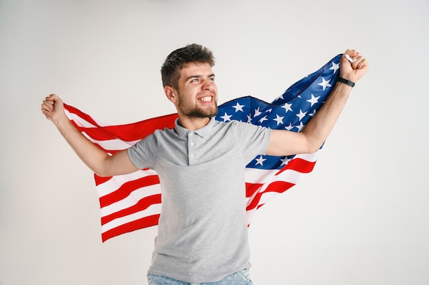 Free photo celebrating an independence day. stars and stripes. young man with flag of the united states of america isolated on white studio wall. looks crazy happy and proud as a patriot of his country.