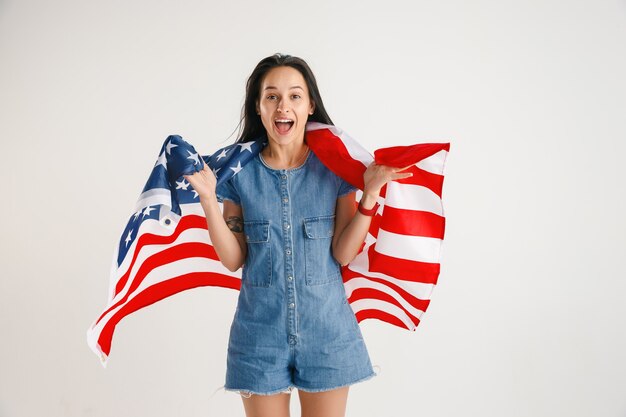 Celebrating an Independence day. Stars and Stripes. Young woman with flag of the United States of America isolated on white studio wall. Looks crazy happy and proud as a patriot of her country.