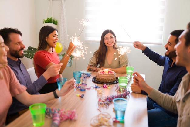 Celebrating together your birthday. Diverse group of friends lighting up sparklers during a party of a smiling young woman and having a lot of fun