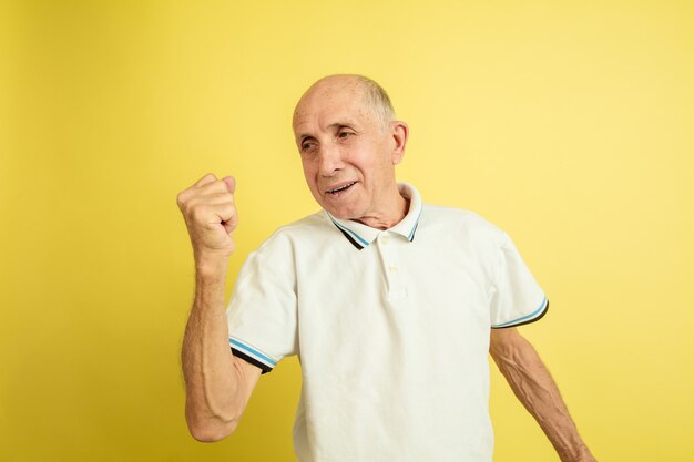 Celebrating win. Caucasian senior man's portrait isolated on yellow studio background. Beautiful male emotional model. Concept of human emotions, facial expression, sales, wellbeing, ad. Copyspace.