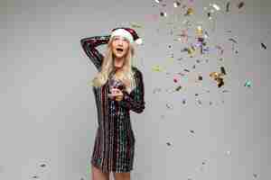 Free photo celebrating xmas and new year, young beautiful surprised girl in santa hat with colourful confetti and champagne.