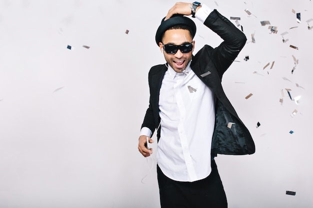 Free photo celebration, party time, happy weekends of excited handsome guy in suit, hat, black sunglasses having fun in tinsels. fashionable look, listening to music, dancer.