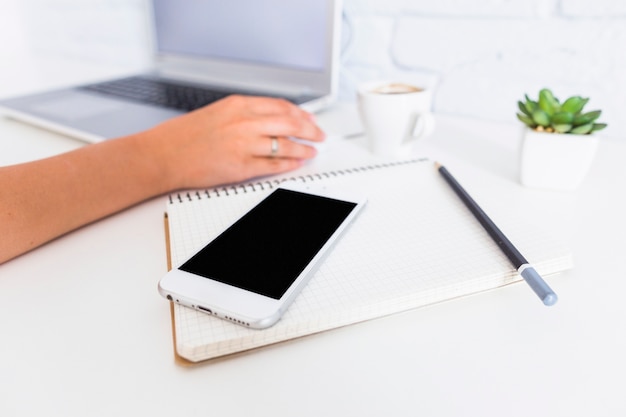 Cellphone, notebook and pencil in front of woman using laptop