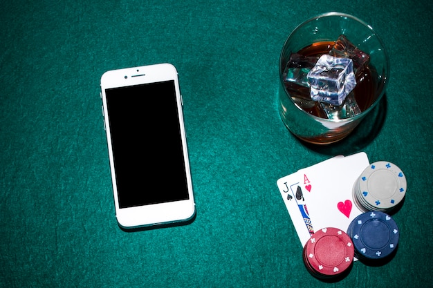 Cellphone and whisky glass with jack of spade and heart ace cards on green poker table