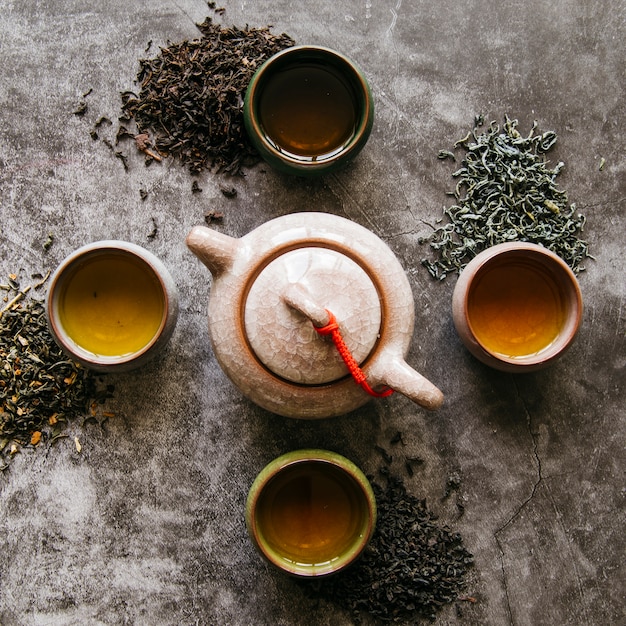 Free photo ceramic clay teapot with dried tea herbs and teacups on dark backdrop