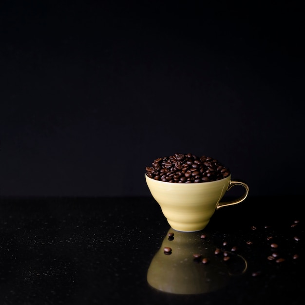 Free photo ceramic cup filled with roasted coffee beans on black background