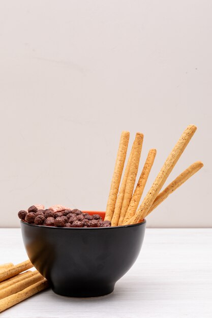 Cereal balls with bread sticks in bowl on white surface