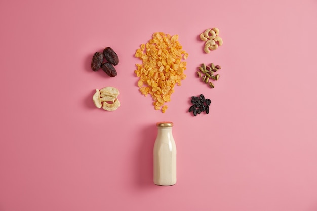 Cereals with dried apples, dates, cashew, pistachio around bottle with milk