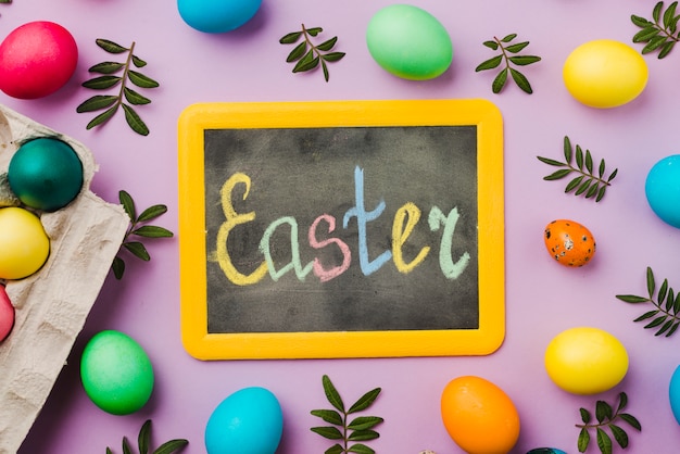 Free photo chalkboard with easter title between set of colored eggs and leaves near container