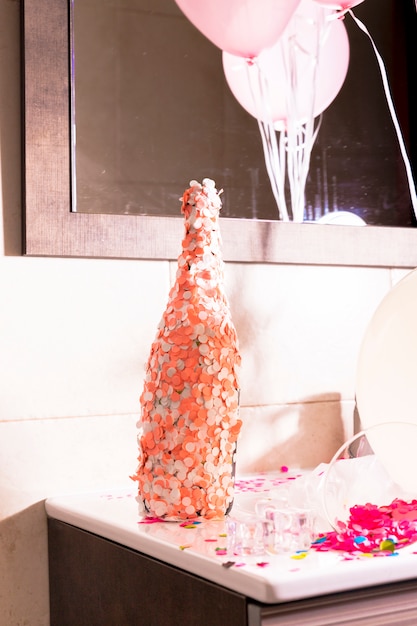 Free photo champagne bottle covered with an orange and white confetti on desk