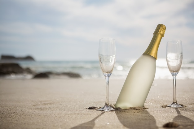 Free photo champagne bottle and two glasses on sand