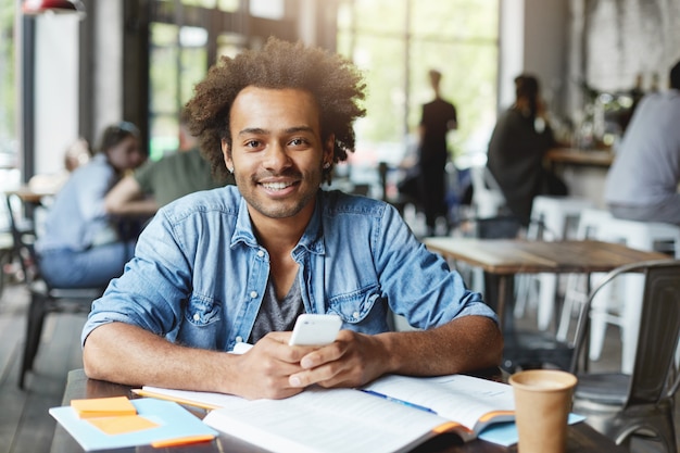 Charismatic good-looking Afro American university student with beard using wireless internet connection on his electronic device during lunch break