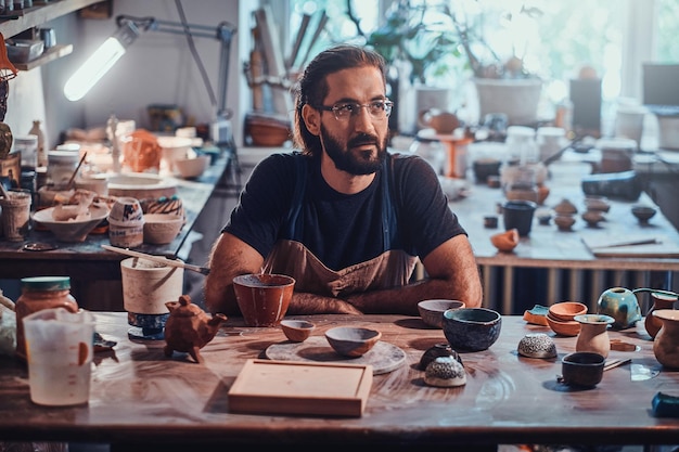 Free photo charismatic happy man in glasses is sitting at his owh workshop and his projects are around him.