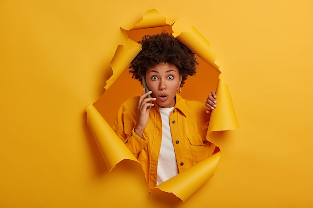 Charismatic impressed African American woman stands in paper hole background