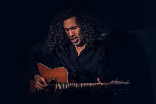 Free photo charismatic rock singer is posing with his guitar while singing at dark studio.