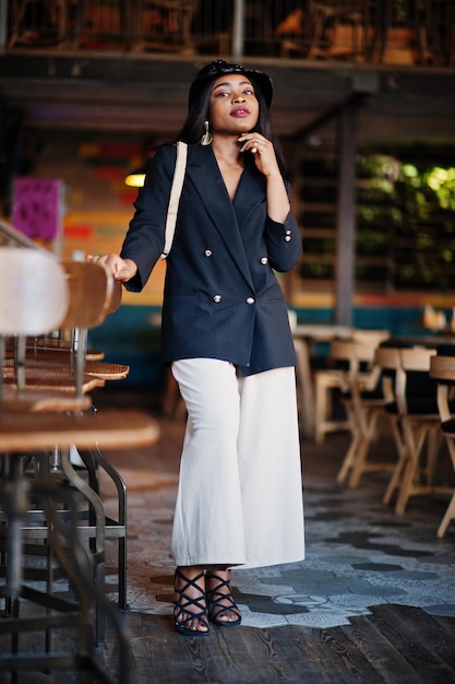 Free photo charming african american woman model in black jacket hat and waist bag relaxing in cafe during free time