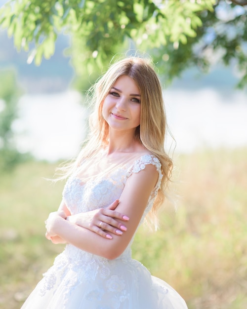 Charming bride looks happy posing in her gorgeous dress outside in a sunny summer day