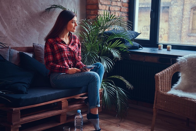 Free photo charming brunette in a flannel shirt and jeans sitting on a couc