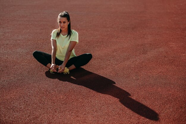 Charming brunette sitting on red court and stretching legs