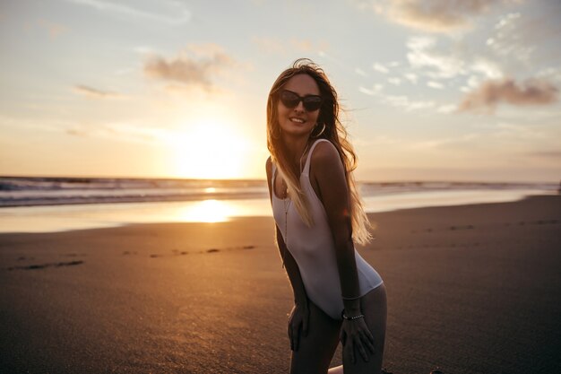 Charming caucasian woman in trendy earrings posing at sandy beach in vacation.