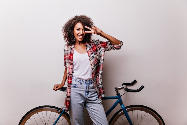 Charming female bicyclist in checkered shirt laughing. Good-humoured woman posing with bicycle and expressing happiness.