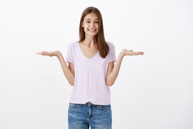 Charming friendly-looking happy woman with short brown hair sprading palms left and right as if holding object over copy space against grey wall