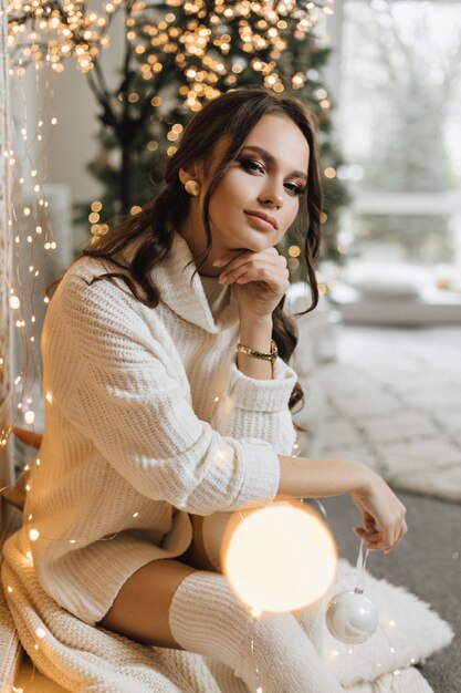 Charming girl in a knitted dress holds a Christmas toy and has dreamy look