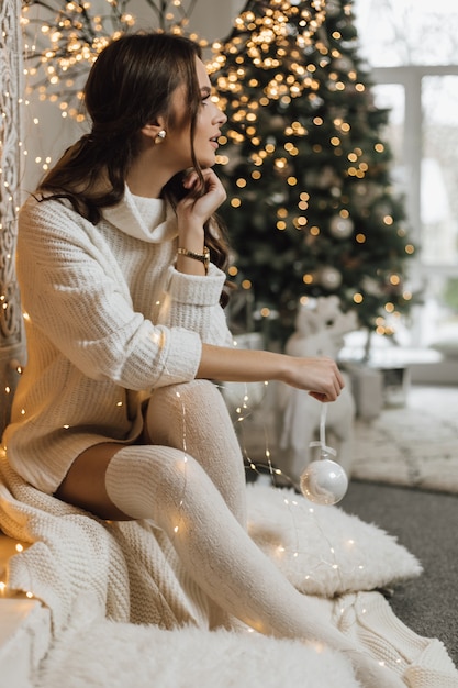 Charming girl in a knitted dress holds a Christmas toy and looks aside