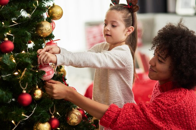 Charming girl and mom decorating Christmas tree