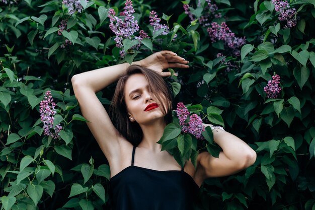 The charming girl stands near bushes with flowers