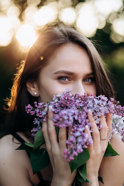 The charming girl stands in the park and keeps a bouquet