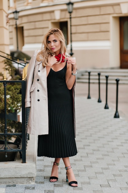 Free photo charming girl with blonde hair walking down the street in black pleated dress ejoying good weather in weekend