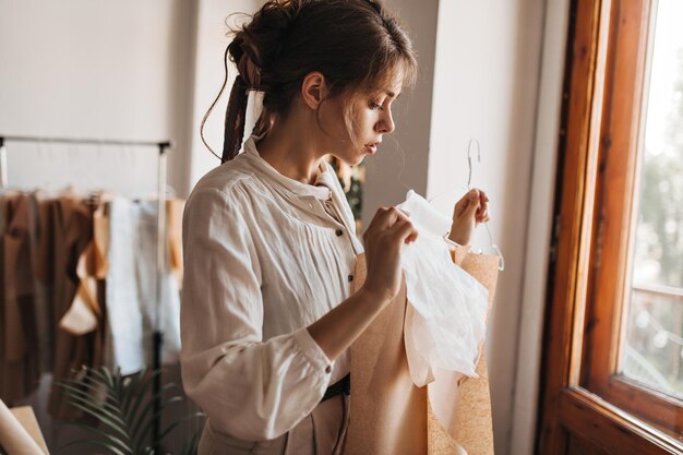 Charming lady looking at her designed clothing Attractive young woman in white blouse works on her new fashion collection