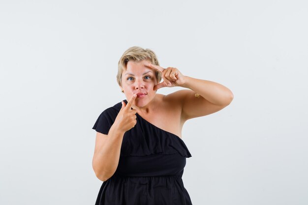 Charming lady pointing at her lip in black blouse and looking concentrated 