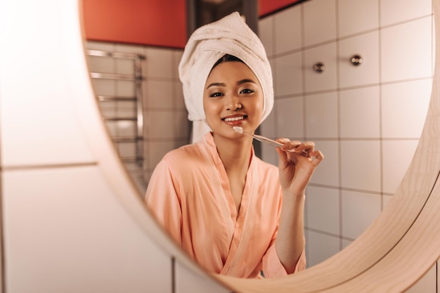 Charming lady in towel looks in mirror and cleans her teeth in bathroom